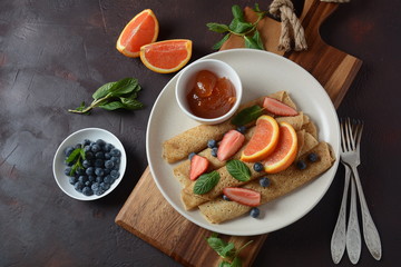 Fototapeta na wymiar Sweet pancakes wrapped with fresh mint, strawberries, blueberries, oranges and jam. Healthy breakfast concept
