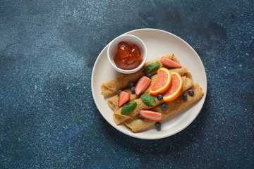 Sweet pancakes wrapped with fresh mint, strawberries, blueberries, oranges and jam. Healthy breakfast concept