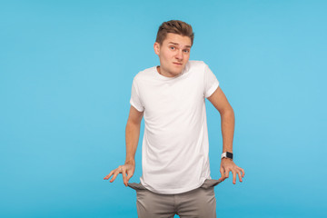 Poor student. Upset man in casual white t-shirt holding empty pockets inside out, showing no money...