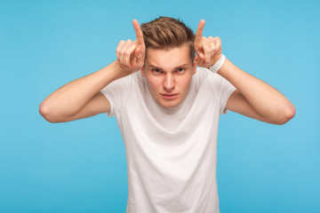 I'm dangerous! Portrait of angry man in white t-shirt threatening to camera with bull horn gesture...