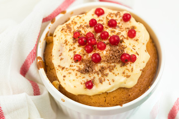 Summer Home pastries: cupcake in round ceramic shape is decorated with red currant berries and cream sauce. Cotton white towel with red stripe, top view