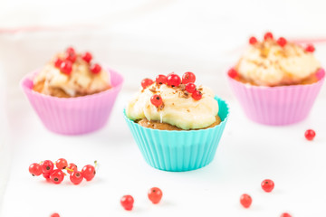 Summer seasonal Home pastries: a group of muffins in silicone form of red and blue flowers, decorated with red currant berries and cream sauce. Individual berries against the background.