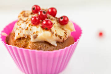 Summer seasonal Home pastries: cupcake in silicone shape is decorated with red currant berries and cream sauce. Maffins in pink individual form for baking.  berries against the background.