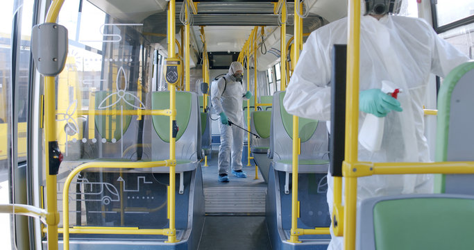 HazMat team in protective suits decontaminating public transport, bus interior during virus outbreak