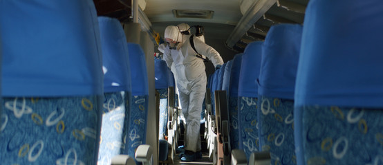 HazMat team in protective suits decontaminating public transport tourist bus interior during virus...