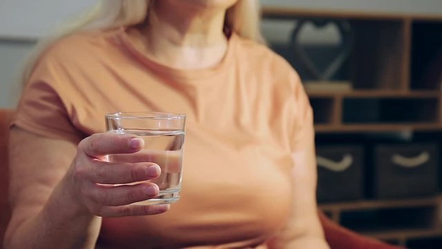 Senior woman with glass of water suffering from Parkinson syndrome, closeup