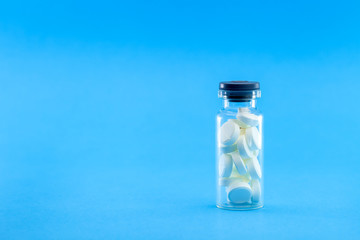 full glass bottle with white pills on a blue background, conceptual medical background with copy space.