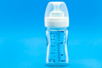 glass bottle with a measuring scale and a silicone pacifier for feeding babies, a transparent plastic cap isolated on a blue background with copy space.