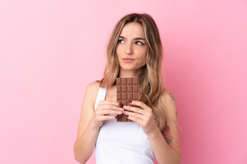 Young woman over isolated pink background taking a chocolate tablet and having doubts