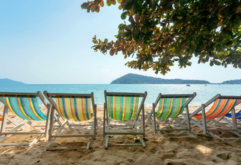 Line of colorful sun lounges on tropical island beach. Some deck chair for relaxing tourists near sea