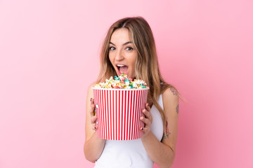 Young woman over isolated pink background holding a big bucket of popcorns