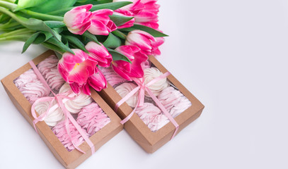 A box of sweets and a bouquet of flowers on a white background. Homemade marshmallows and tulips