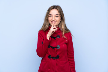 Young woman with winter coat over isolated blue background doing silence gesture