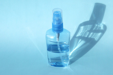 A bottle of antiseptic antibacterial spray stands on a blue background with a beautiful shadow from the sun. Selective focus