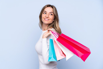 Young woman over isolated blue background holding shopping bags and looking back