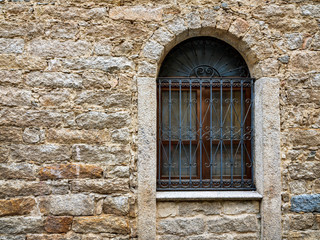 Arched window with wrought iron grate and ancient wall built with stones of various types and thickness