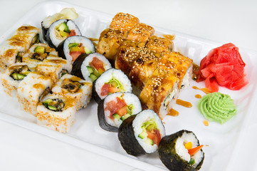 Set of sushi and rolls of three types with wasabi and ginger root on a disposable plastic plate