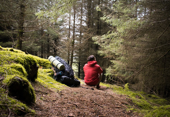 Senderista descansando en el bosque con su gran mochila en el suelo