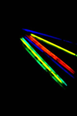 Bright neon colored glow sticks on a black background. Light in the dark. Copy space.