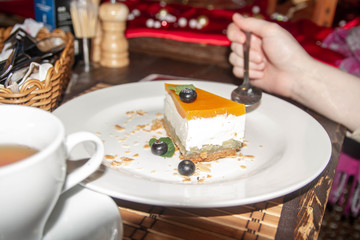 Pear cheesecake with blueberries on a plate in a restaurant. A girl eats dessert with a spoon in a cafe. Tea in the restaurant.