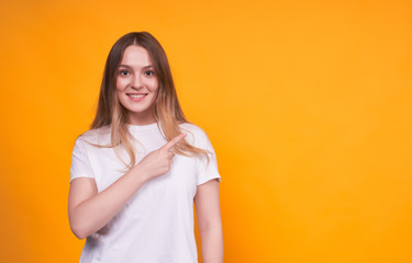 Obraz premium Young smiling emotional girl shows aside on a yellow wall back