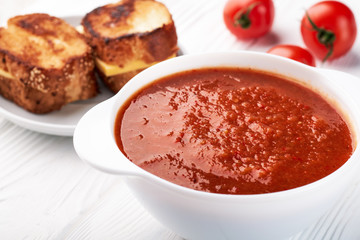 A bowl of tomato soup sandwiches with cheese and fresh tomatoes on the table