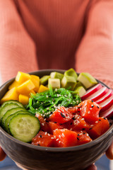 Girls' hands holding salmon poke bowl with salad, avocadowith salmon, avocado, rice. Traditional Hawaiian dish