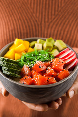 Girls' hands holding salmon poke bowl with salad, avocadowith salmon, avocado, rice. Traditional Hawaiian dish