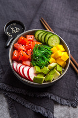 Salmon poke bowl (avocado, salmon, cucumber, radish and rice) on dark background , top view. Asian trendy food