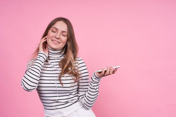 Happy cheerful girl in headphones and a phone on a pink background.
