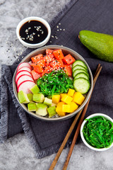 Salmon poke bowl (avocado, salmon, cucumber, radish and rice) on dark background , top view. Asian...