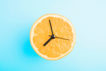 Fresh orange with clock arrows. Healthy nutrition/healthy lifestyle concept on blue background.