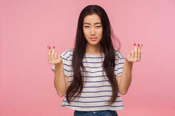 Give me payment. Portrait of attractive asian girl with brunette hair in striped t-shirt showing money gesture, demanding financial help, asking reward. indoor studio shot isolated on pink background