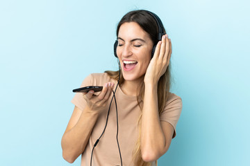Young caucasian woman isolated on pink background listening music with a mobile and singing