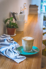 a cup of latte with milk on a cafe counter with saucer and tea spoon and napkin