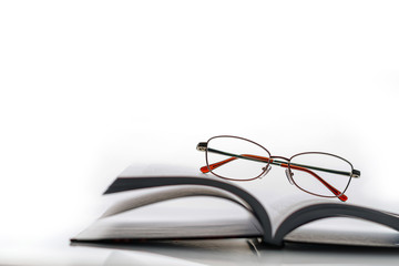 Composition with an open book and glasses on a white background with space for text.