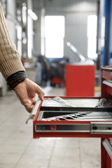 A set of tools for repair in car service. Wrench kit. Professional red toolbox. Mechanic taking facilities from special box for mechanical instruments. Mechanic looking for spanner
