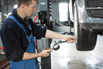 Mechanic checking tire pressure in car wheel at service station