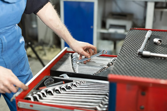 A set of tools for repair in car service. Wrench kit. Professional red toolbox. Mechanic taking facilities from special box for mechanical instruments. Mechanic looking for spanner