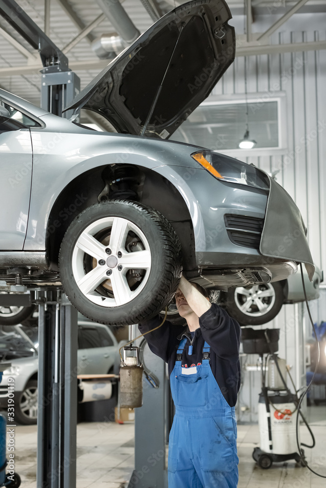 Wall mural European mechanics in uniform is working in auto service with lifted vehicle. Car dealer repair and maintenance in the auto repair center.