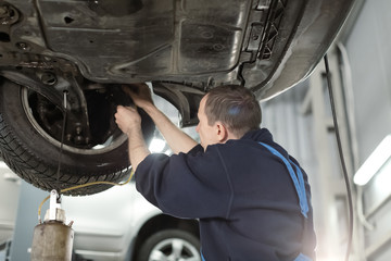 Mechanic examining under car at the repair garage. Car service mechanic repairing and maintenance. Auto mechanic man or smith with wrench at workshop