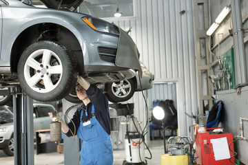 Mechanic checking oil level in car engine. Automobile on mechanical lift. Special equipment for diagnostic. Service station and machine maintenance concept