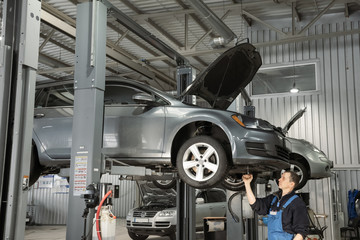 European mechanics in uniform is working in auto service with lifted vehicle. Car dealer repair and maintenance in the auto repair center.