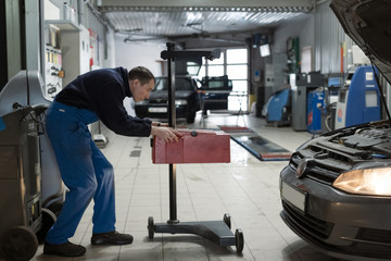 Modern car at a service station. Repairman is adjusting the headlight. He use special professional equipment. A close-up shows a headlight. Spare parts, service, repair concept.