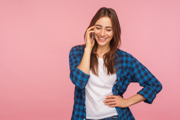 Mobile communication. Happy smiling girl in checkered shirt calling to friend telling good news, expressing positive emotions while talking on cellphone. indoor studio shot isolated on pink background