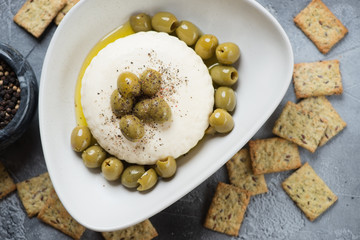 Green olives and soft cheese with black pepper, olive oil and crackers, view from above, closeup