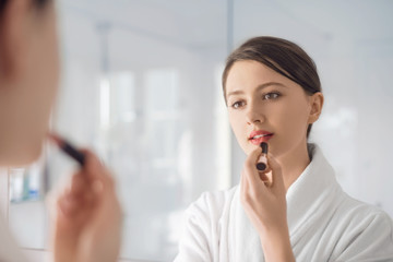 A young woman putting on lipstick