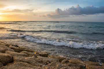 Sunshine from sundown on the stones of the seashore with waves and horizon during the summer time in Bali