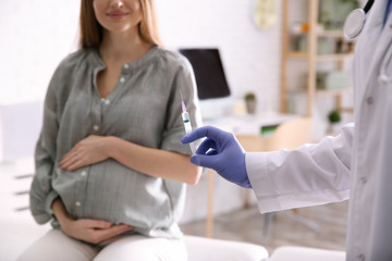 Doctor giving injection to pregnant woman in hospital, closeup. Vaccination concept
