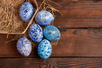 Blue cosmos chicken eggs lie in round wooden basket which stands on a dark wooden table.